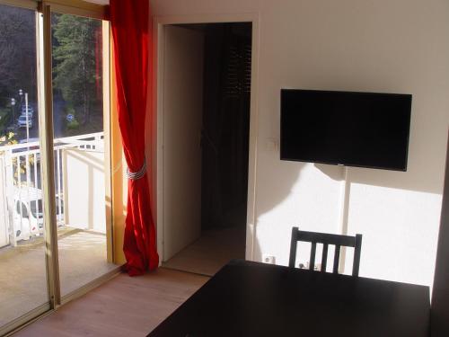 a room with a table and a television and a door to a balcony at T2 bis Capvern les Bains , calme , face au parc thermal in Capvern