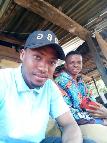 a man wearing a hat sitting next to another man at MAKENI CITY in Kamakwie