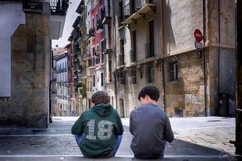two young men sitting on a city street at TOP APARTMENT ÁTICO con TERRAZA con vistas al ENCIERRO SAN FERMÍN in Pamplona
