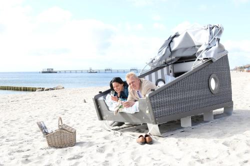 a man and a woman sitting in a bed on the beach at Schlafstrandkorb Nr 3 in Kellenhusen
