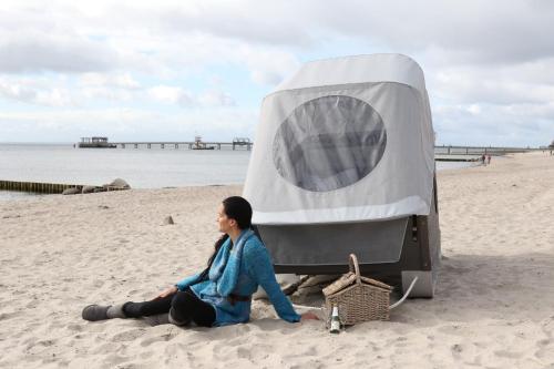 a woman sitting on the beach next to a tent at Schlafstrandkorb Nr 3 in Kellenhusen