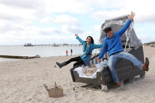 Un uomo e una donna seduti su una valigia sulla spiaggia di Schlafstrandkorb Nr 1 a Kellenhusen