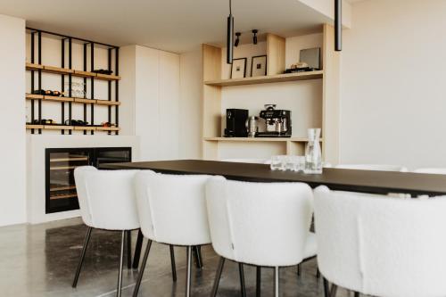 a kitchen with a bar with white chairs at Stil 1827 in Sint-Laureins