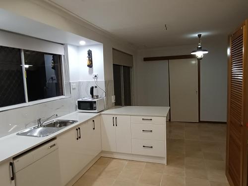 eine weiße Küche mit einer Spüle und einer Mikrowelle in der Unterkunft Comfort and Convenient in Perth