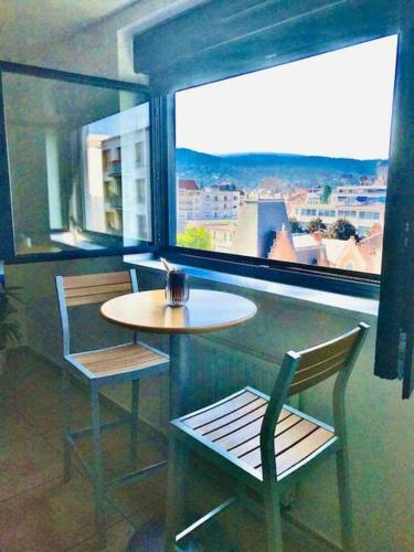 une table et des chaises dans une pièce avec une grande fenêtre dans l'établissement Mon nuage de Jaude, à Clermont-Ferrand