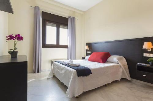 um quarto com uma cama com uma almofada vermelha e uma janela em Disfruta Sevilla, Recepción 24 h, Apartamento EL MIRADOR em Bormujos