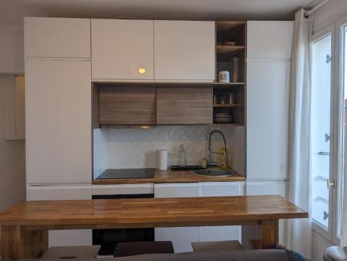une cuisine avec des armoires blanches et une table en bois dans l'établissement Escapade à 2 ou en petit groupe Appartement tout équipé Quartier résidentiel calme RER direct Parfait pour télétravail et détente, à Saint-Maur-des-Fossés