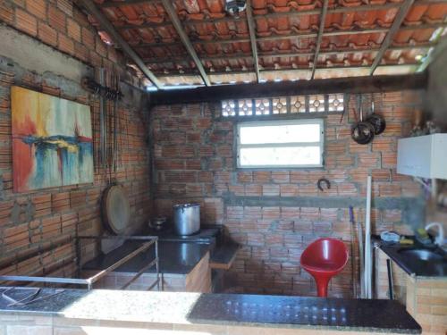 una cocina con una pared de ladrillo y un taburete rojo en Casa c/Piscina em Arroio do Rosa en Imbituba