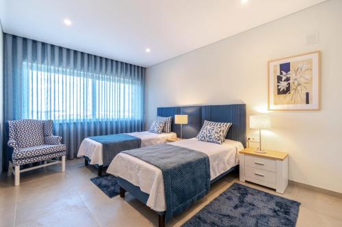 a bedroom with two beds and a chair and a window at Holiday House Beach Porto Mós by Villas Key in Lagos
