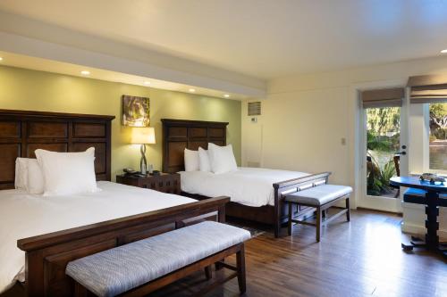 a bedroom with two beds and a desk and a window at The Quail Lodge in Carmel