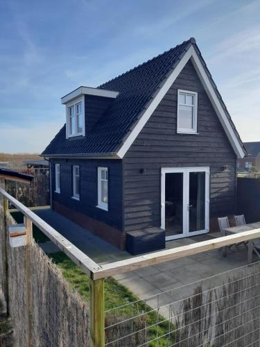 a small black house with a wooden deck at Vakantiewoning Nimmerdor, Grijpskerke, dichtbij strand en stad in Grijpskerke