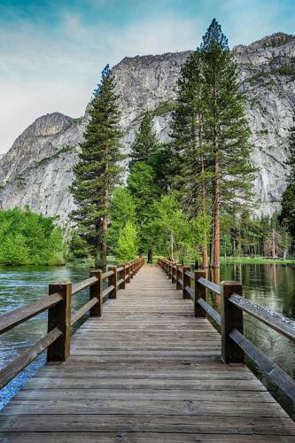 a wooden bridge over a lake with a mountain in the background at Under Canvas Yosemite in Groveland