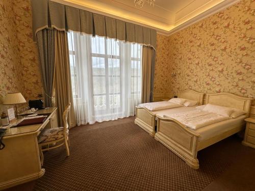 a bedroom with a bed and a desk and a window at Hotel Château Cihelny in Karlovy Vary