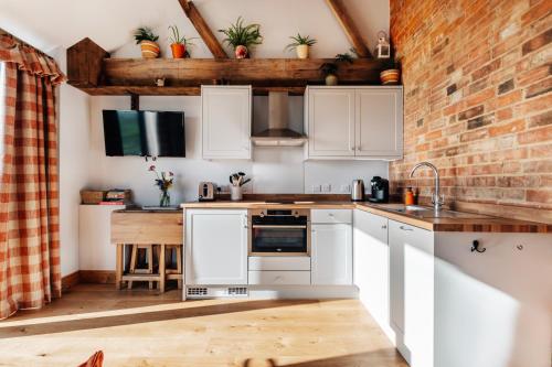 a kitchen with white cabinets and a brick wall at The Linhay in Peterborough