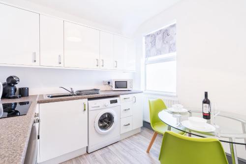 una cocina con armarios blancos y una mesa con sillas verdes en The Urban Apartment, en Doncaster