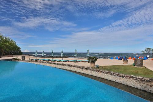 a large swimming pool next to a beach with umbrellas at JW Marriott Guanacaste Resort & Spa in Tamarindo