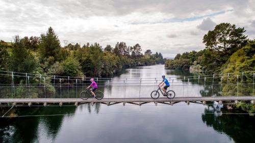 two people riding bikes on a bridge over a river at Cosy on Korari in Mangakino in Mangakino