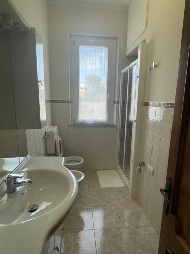 une salle de bains blanche avec deux lavabos et une fenêtre dans l'établissement Appartamento - Porto San Giorgio, à Porto San Giorgio