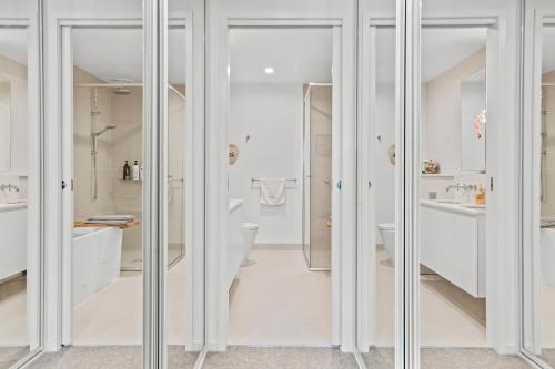 a white bathroom with glass doors and a toilet at StayAU Modern 2BR Townhouse w/ pool in Oakleigh