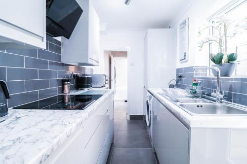 a white kitchen with blue tiles and a sink at Great 3 Bed Refurbished House in Colchester