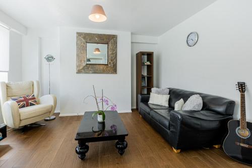 sala de estar con sofá de cuero negro y guitarra en Charming 1 Bedroom Serviced Apartment in Camden, en Londres