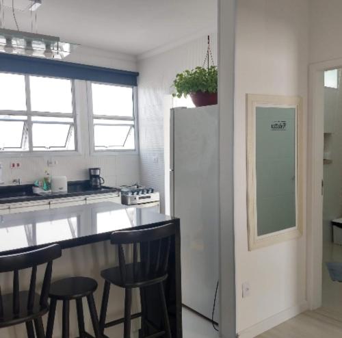 a kitchen with a counter with stools and a refrigerator at Apt Guarujá Enseada lado praia FAN 1 dorm Tv Netflix Wi-Fi Ar até 5 pessoas in Guarujá