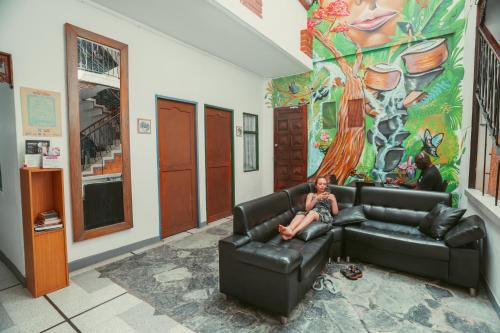 une femme assise sur un canapé dans une pièce avec une fresque dans l'établissement Hostal Pura Vida la 70, à Medellín