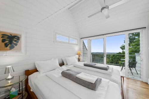 a white bedroom with two beds and a large window at Sunrise House in Hazelbrook