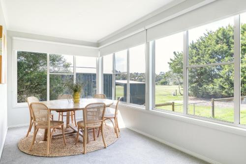 ein Esszimmer mit einem Tisch, Stühlen und Fenstern in der Unterkunft Red Rocks Golf & Accommodation - Phillip Island in Cowes