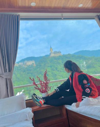 a woman sitting on a bed looking out of a window at Ruby Tam Đảo in Tam Ðảo