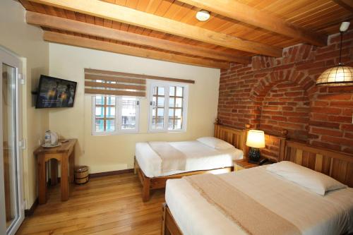a bedroom with two beds and a brick wall at Hotel Boutique Vieja Cuba in Quito