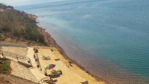 a beach with chairs and an umbrella in the sand at Comfy Stays Sea View Apartments at DeadSea Samarah Resort in Sowayma