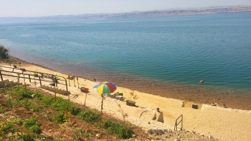 a beach with an umbrella next to the water at Comfy Stays Sea View Apartments at DeadSea Samarah Resort in Sowayma