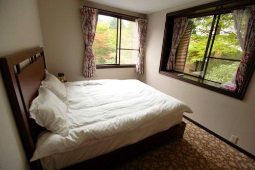 a bedroom with a white bed with two windows at 箱根温泉ヴィラ 源泉かけ流し bbq付き グループ宿泊に最適 in Hakone