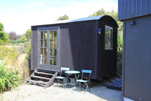 ein schwarzes kleines Haus mit einem Tisch und Stühlen in der Unterkunft The Bird Hide - rustic luxury by the water in Dunedin