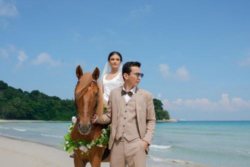 a bride and groom with a horse on the beach at Indra Maya Pool Villas in Lagoi
