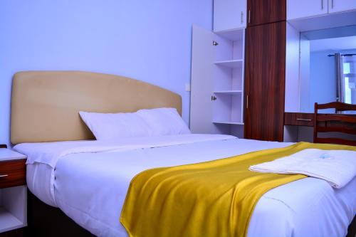- une chambre avec un grand lit blanc et une couverture jaune dans l'établissement Kechei Centre, à Iten