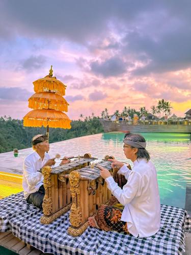 two people sitting at a table in front of the water at Kastara Resort in Ubud