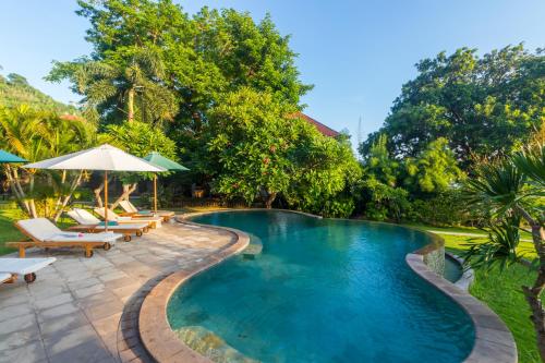 a pool with chairs and umbrellas next to a resort at Villa Sky Dancer - Bali in Amed