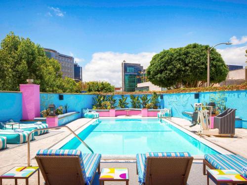 a large swimming pool with chairs and a blue wall at Hotel Sofitel Los Angeles at Beverly Hills in Los Angeles