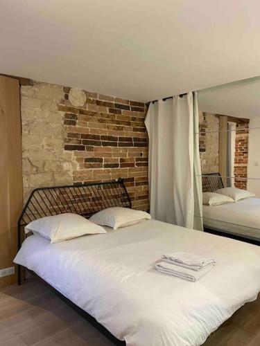 une chambre avec un grand lit blanc avec un mur de briques dans l'établissement Appartement de charme en plein cœur de Paris, à Paris