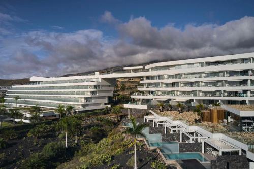 a large white building on a hill with palm trees at Royal Hideaway Corales Beach - Adults Only in Adeje