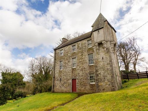 an old stone building with a red door on a hill at CLIFF River Lodge - Luxury Fishing Lodge in Ballyduff