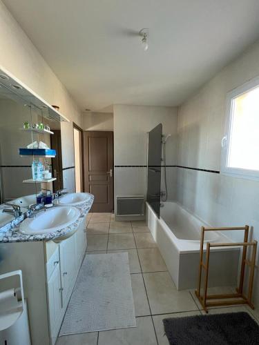 ein Badezimmer mit zwei Waschbecken, einer Badewanne und einer Dusche in der Unterkunft Maison avec piscine entièrement climatisée in Sauvian