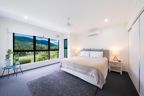 a bedroom with a bed and a large window at Whitsunday Whisper Terrace - Townhouse Pets Airlie in Airlie Beach