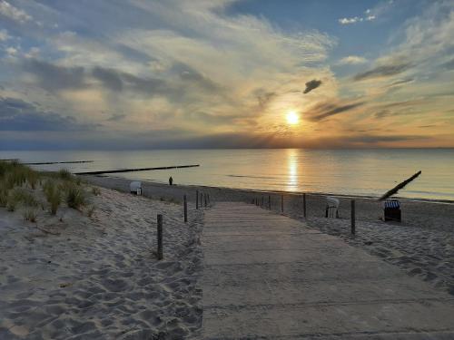 un camino en la playa con la puesta de sol sobre el agua en Eikkater 4 EG, en Graal-Müritz