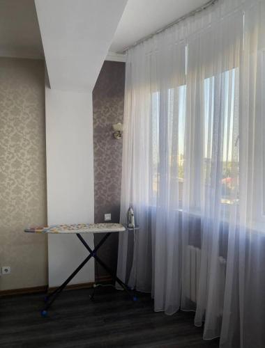 een kamer met een raam met witte gordijnen en een tafel bij Уютный уголок в центре города in Bisjkek