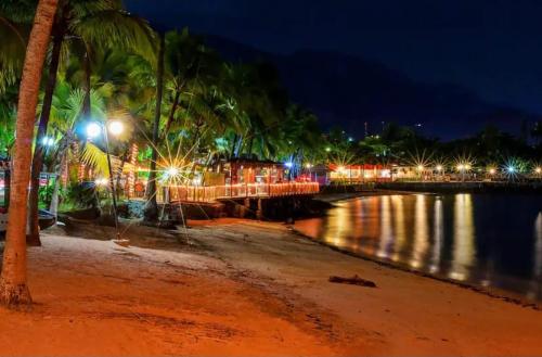 a beach with palm trees and lights at night at Casas MDP ilhabela/2 in Ilhabela