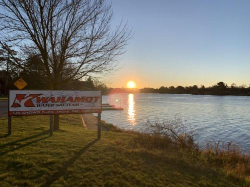 a sign in front of a lake with the sunset at Bridge Inn Tomahahwk - Room 106 ,1 King Size Bed,1 Recliner, Walkout, River View in Tomahawk
