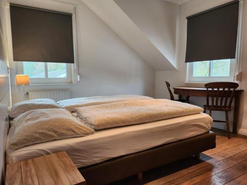 a bed in a room with two windows and a desk at Landhuis de heibloem in Heythuysen